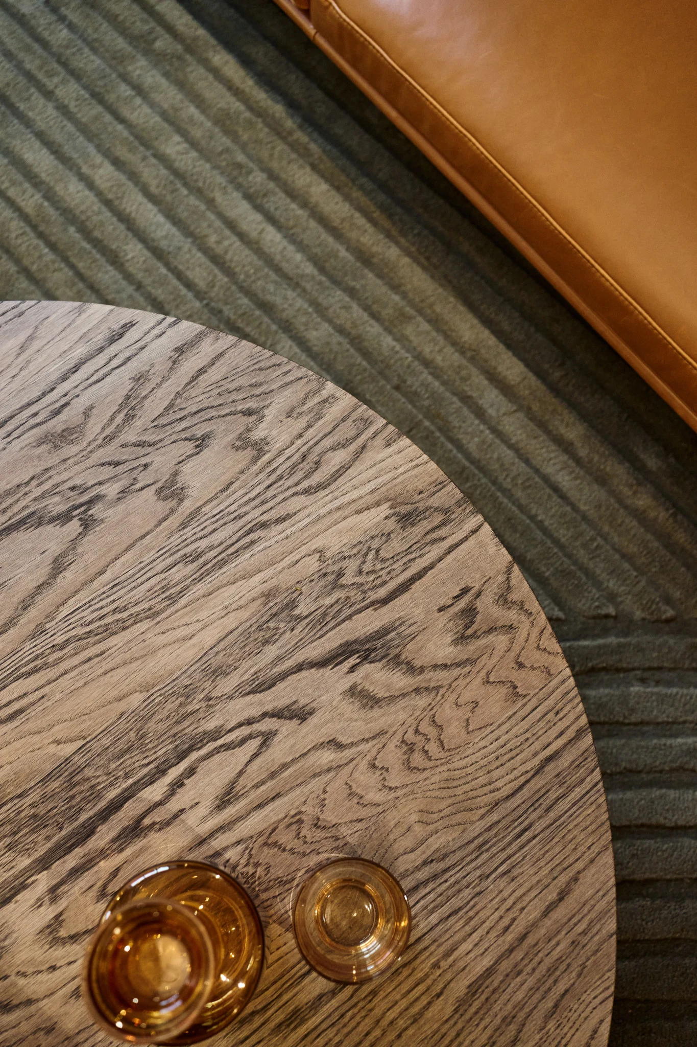 A coffee table with a dark brown table top stands in front of a sofa, with various amber-coloured glasses from the Raise collection by Muuto on top.