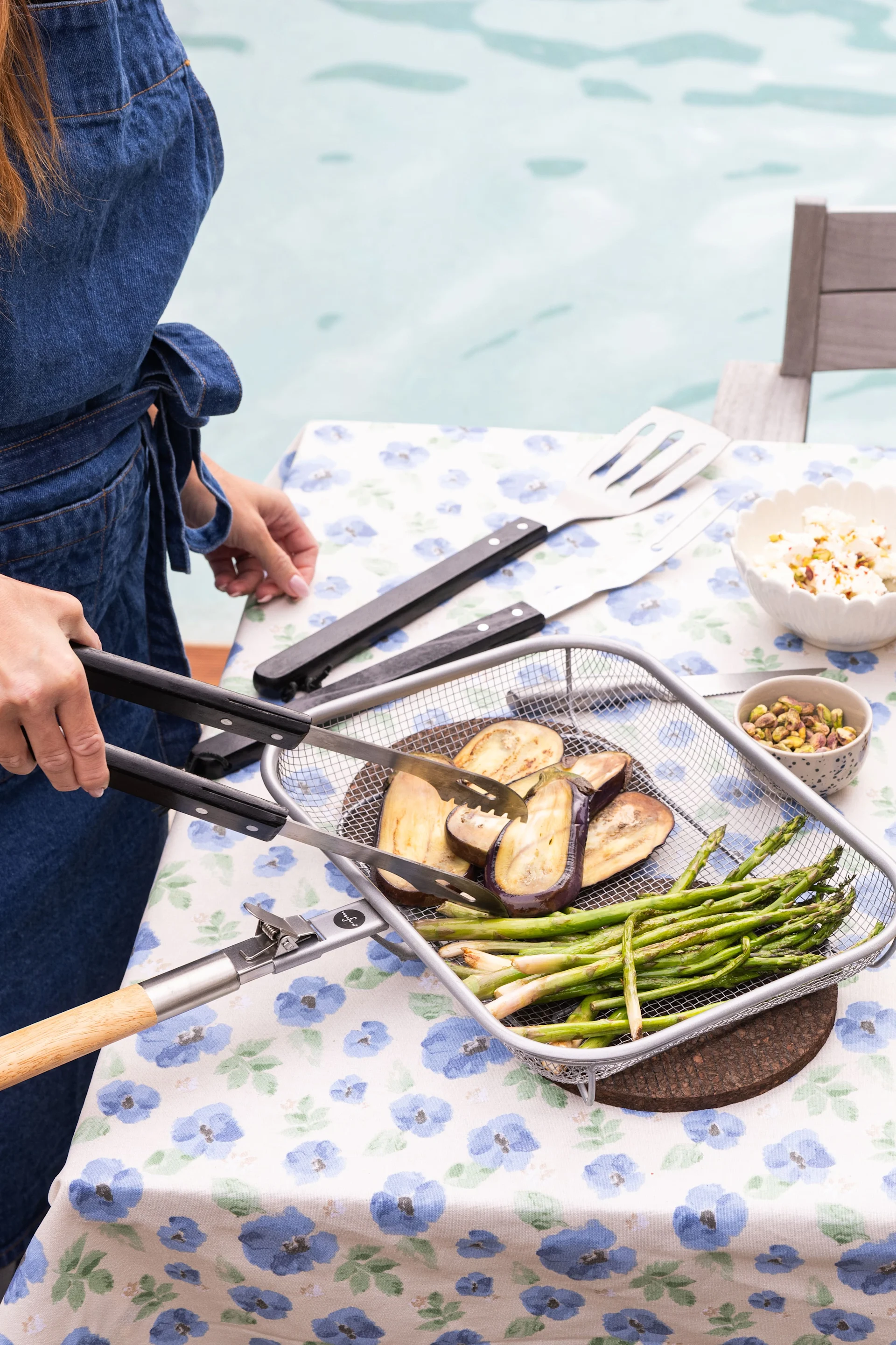 Here you see a woman turning over aubergine and asparagus during a summer bbq.