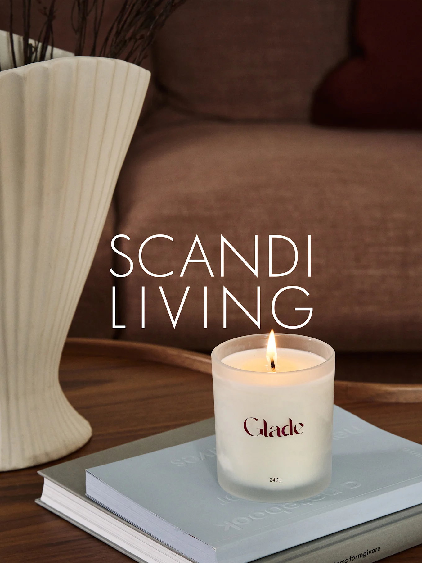 A burning Glade candle on books, next to a ridged vase with branches. Overlay text: SCANDI LIVING.