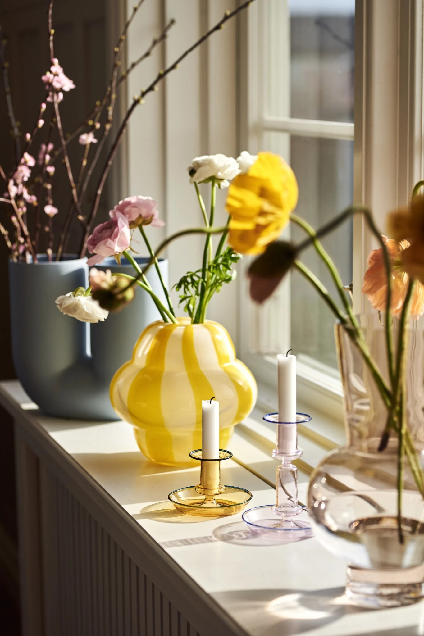 The Curlie vase from Byon in a bright pop of yellow sits on the windowsill along with various other vases and glass candle holders. 
