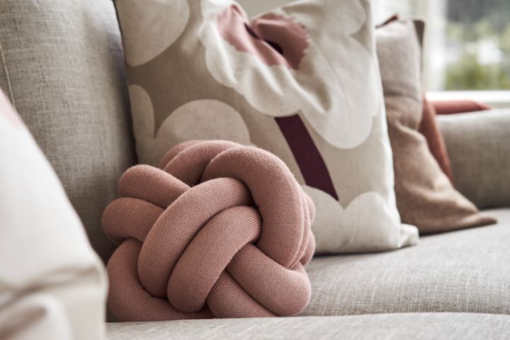 The Knot Cushion small in dusty pink on a sofa with other complementing pillows. 