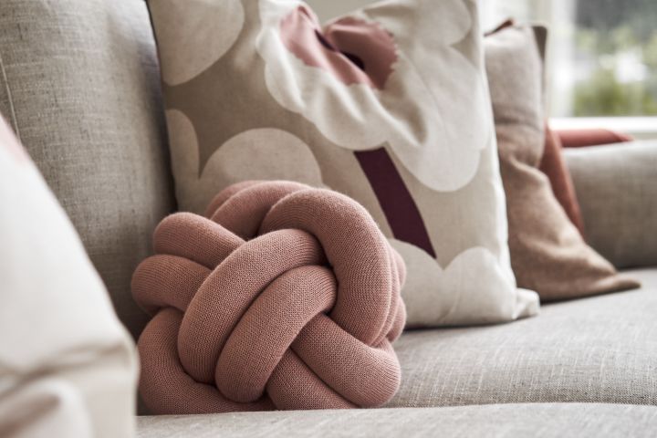 The Knot Cushion small in dusty pink on a sofa with other complementing pillows. 