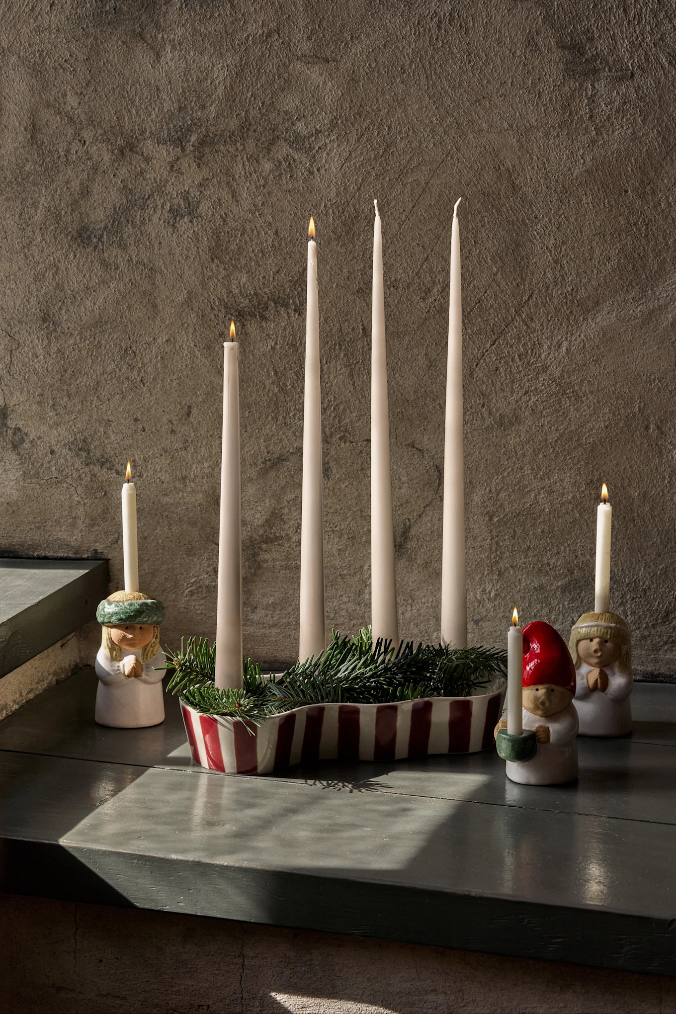 Advent display with four unlit candles, green fir, and three figurines holding lit candles.