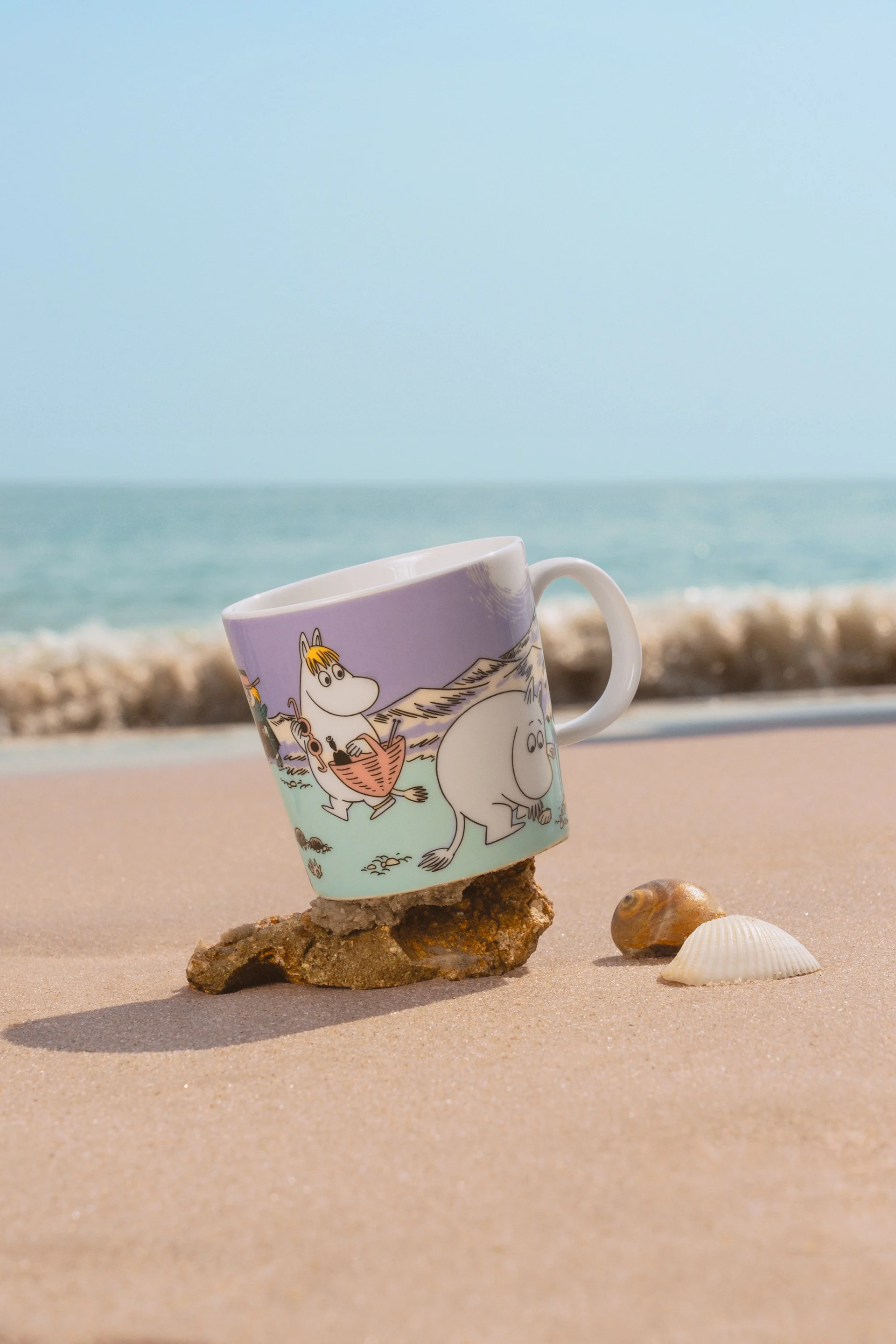 The Moomin mug Summer 2025, ‘Beach Day’ stands on a sandy beach.