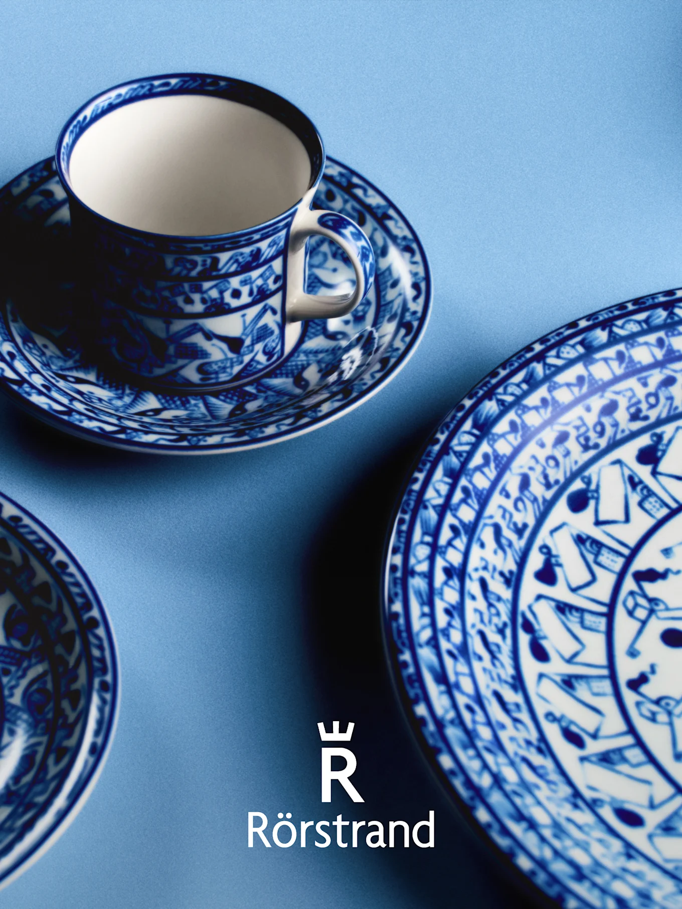 Blue and white patterned teacup, saucer, and plate on light blue, with Rörstrand logo.