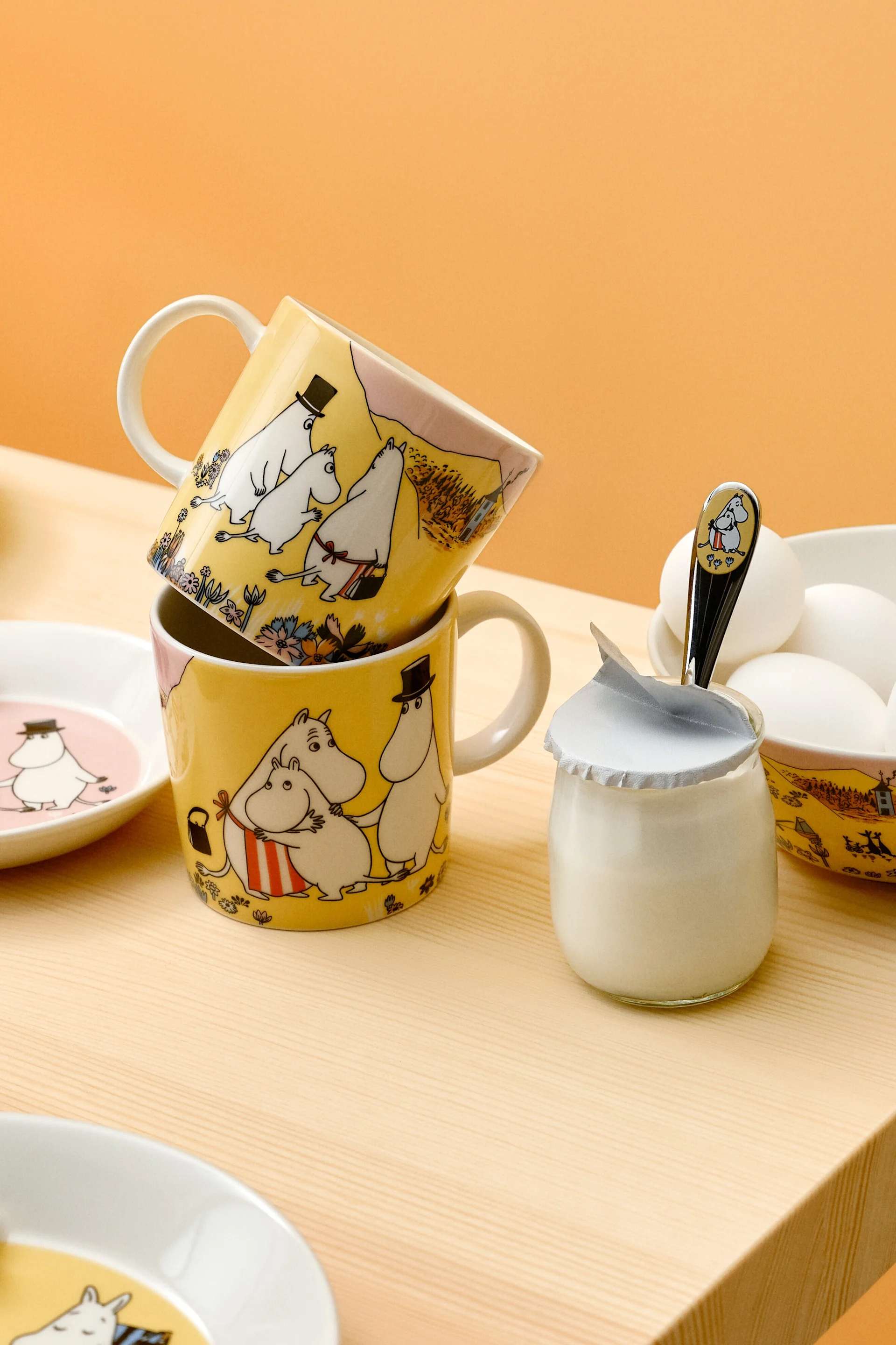 Two Family time Moomin cups are stacked on a laid breakfast table.