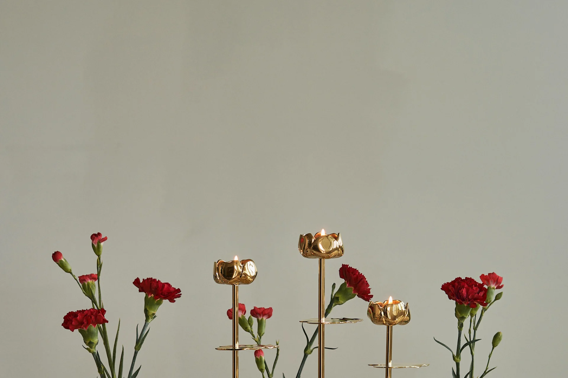 Golden flower-shaped candlesticks with lit candles and red carnations.