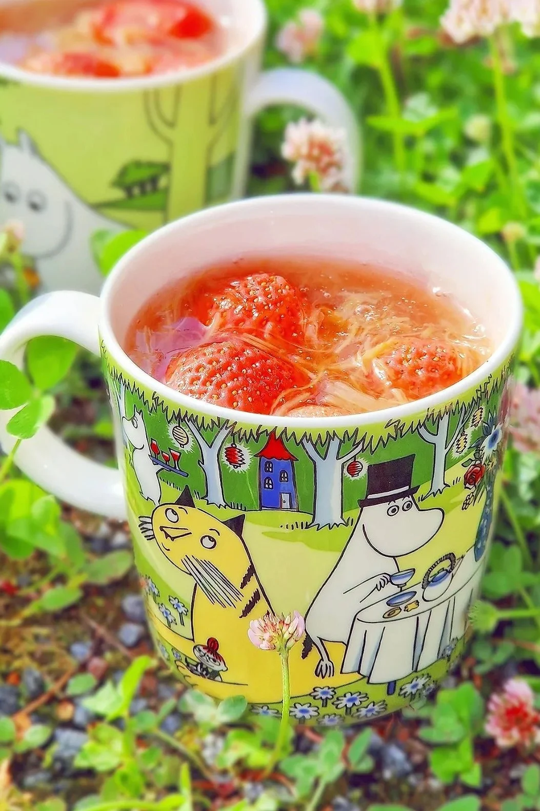 The Moomin mug from summer 2023, ‘Garden Party’, is standing in @jasmiiniflower's garden, filled with raspberries.