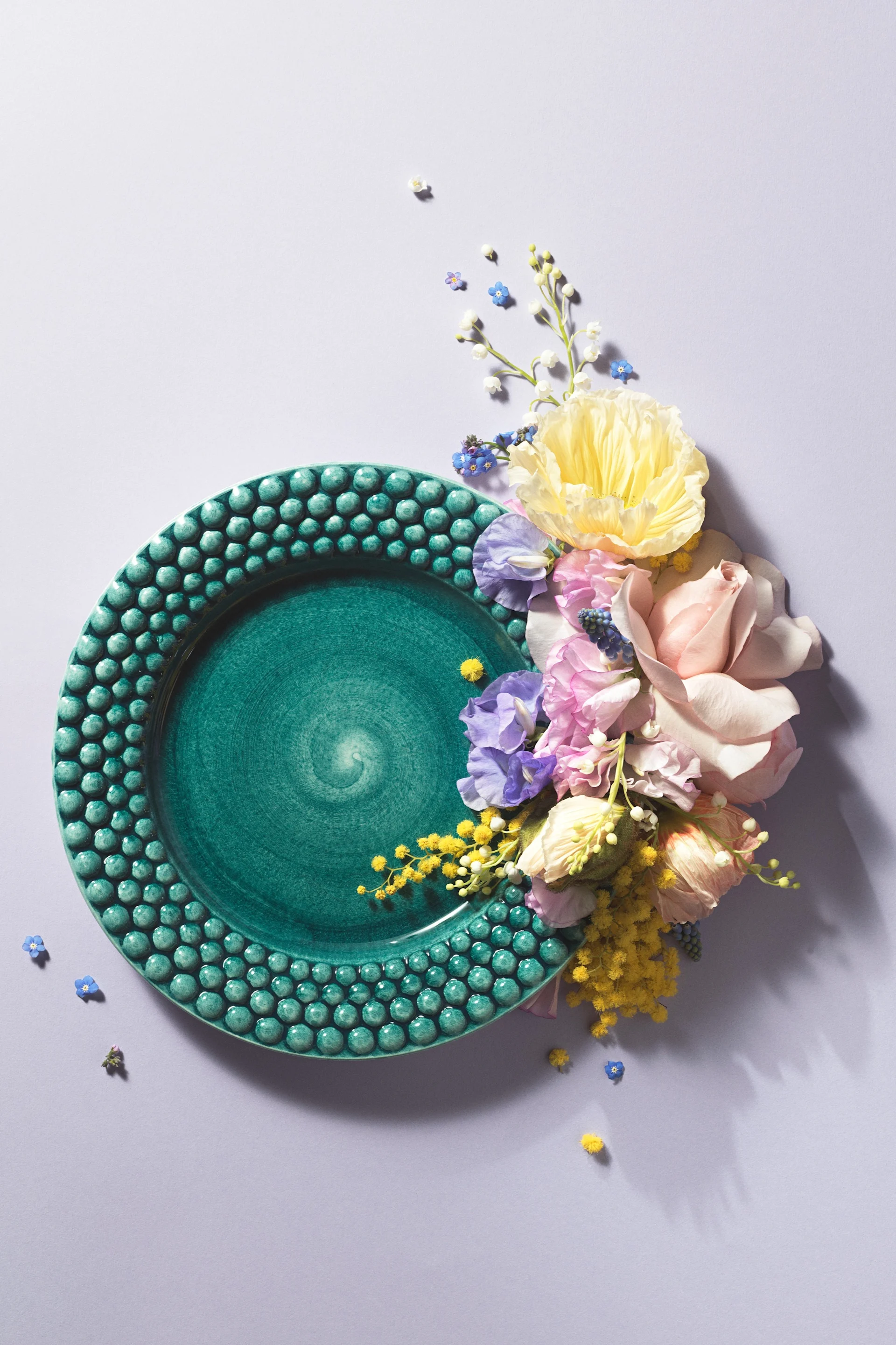 A plate from the Bubbles collection in the colour Ocean by Mateus, artfully staged with flowers for a photo.