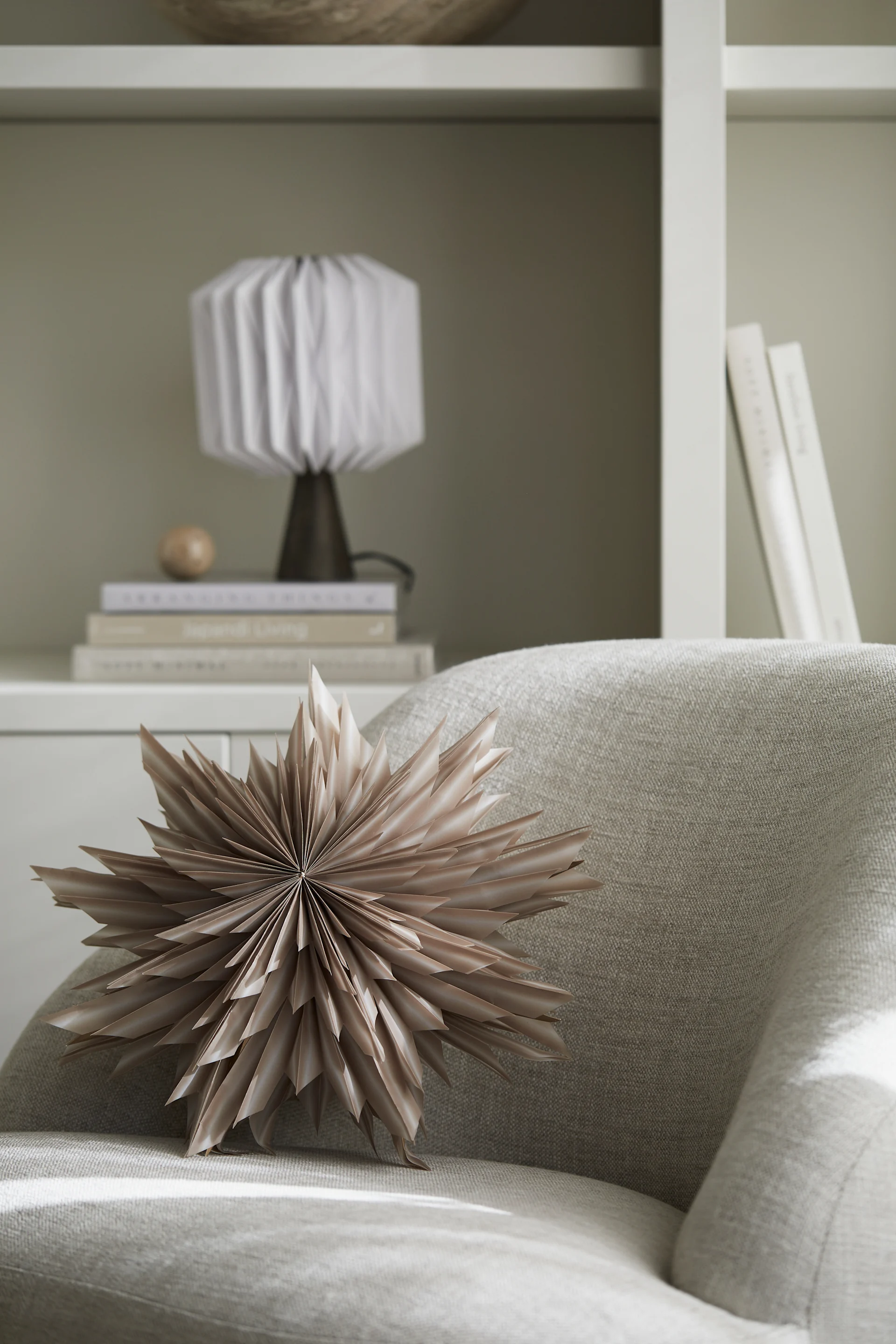 A Christmas paper star lantern - Helena - from Watt & Veke is placed on an arm chair waiting to be hung.  