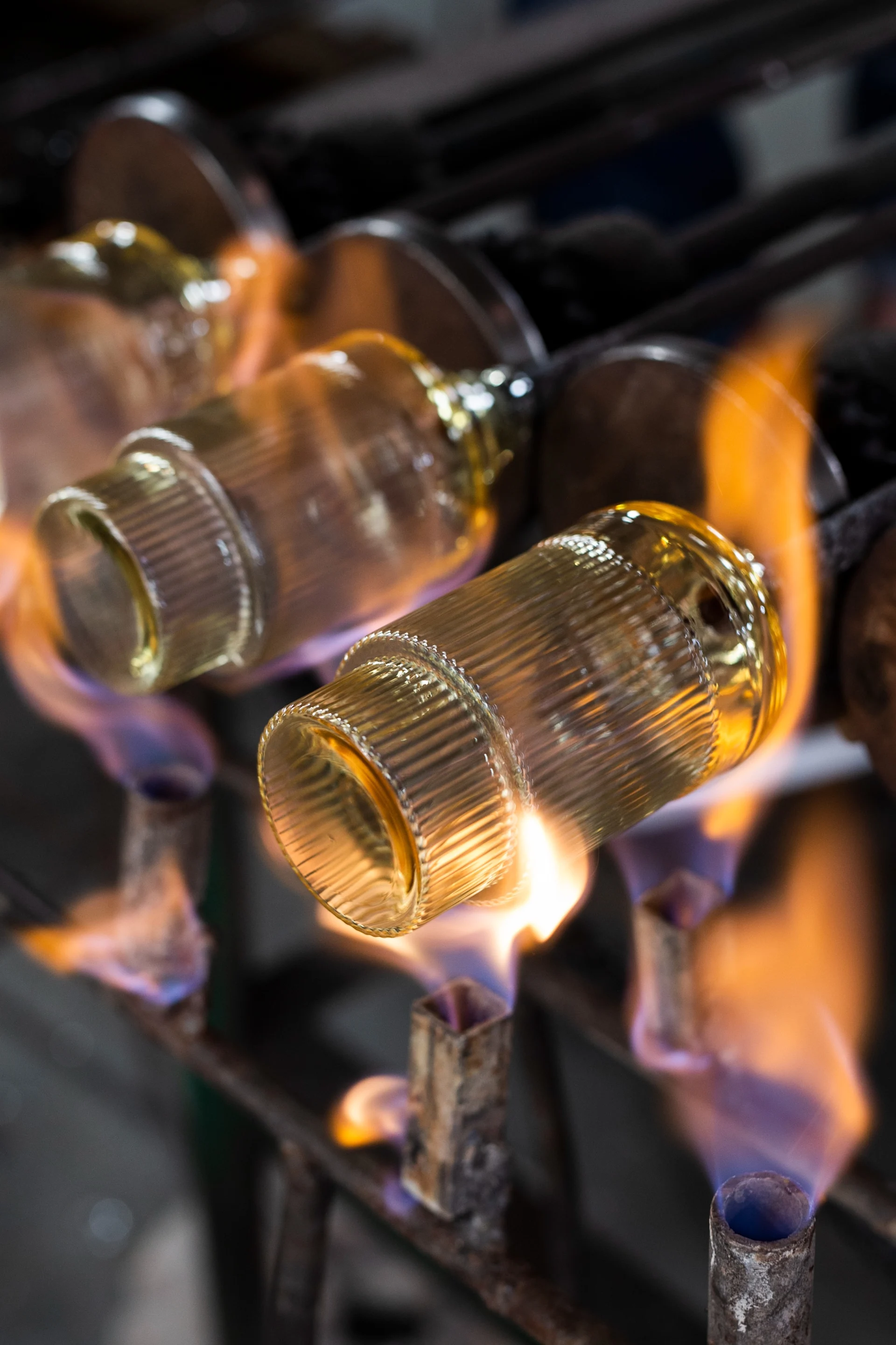 Ribbed golden glass objects being heated by orange and blue flames on a metal rack.