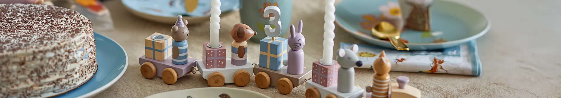 Wooden birthday train with animal figures, pastel gift blocks, candles, and number 3, next to a chocolate-sprinkled cake.