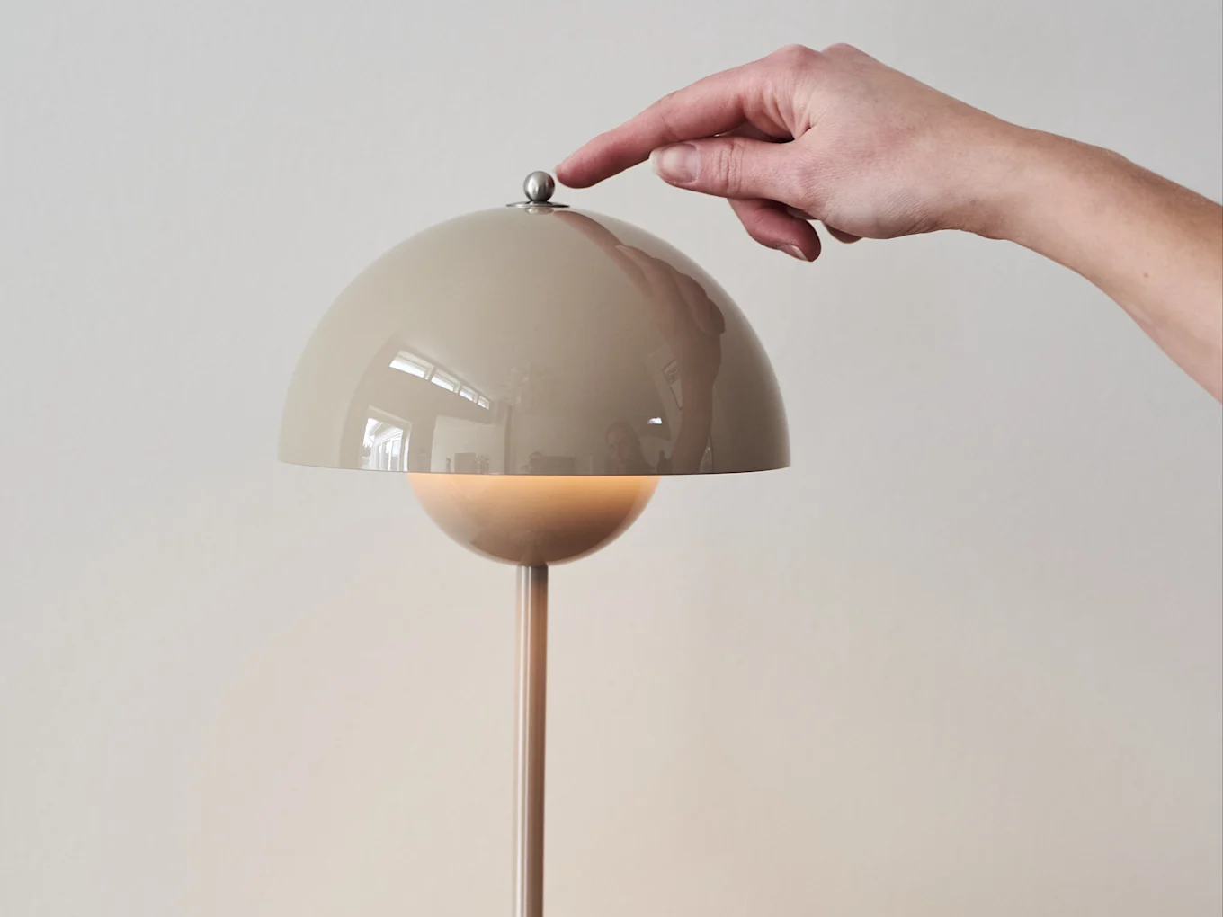 Hand pressing a metallic button on a beige dome-shaped lamp, which emits a warm glow.