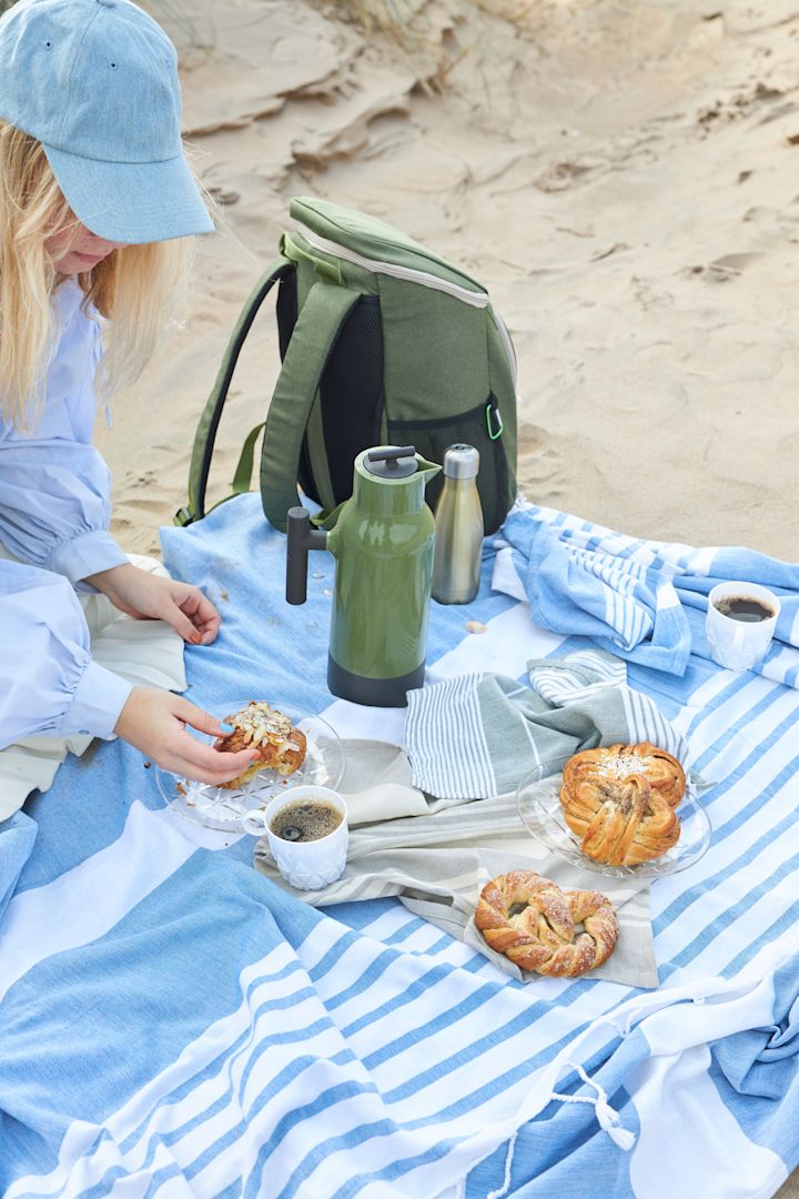 Here you see a woman sitting on a blue striped picnic blanket with a green picnic bag, all from Sagaform. 