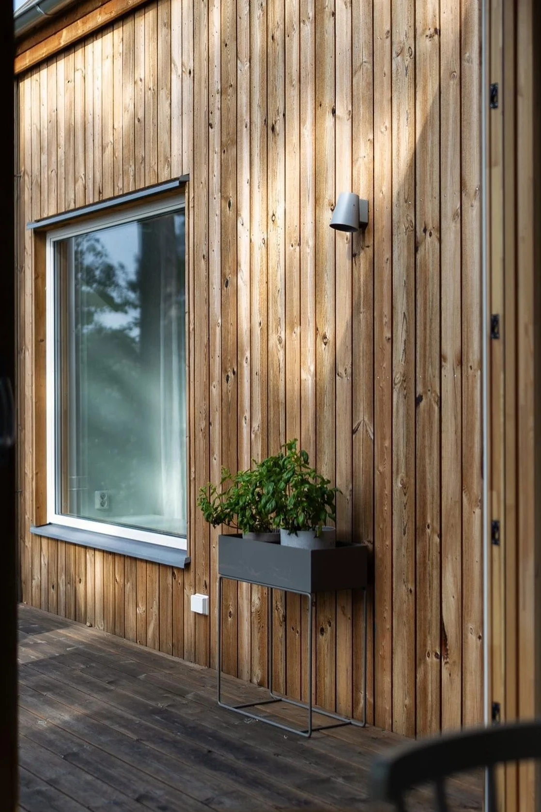 Here you can see the black metal plant box from Ferm Living standing on the terrace of a Swedish wooden house.
