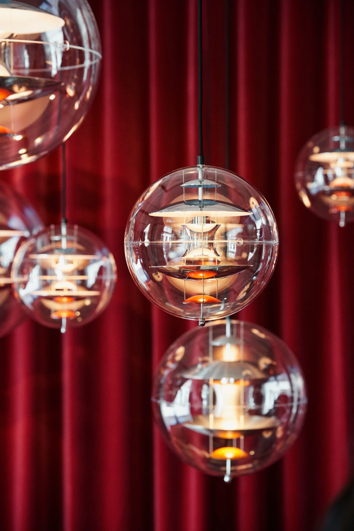 Several Globe Glass pendant lights by Verpan hang from the ceiling in front of a red curtain.