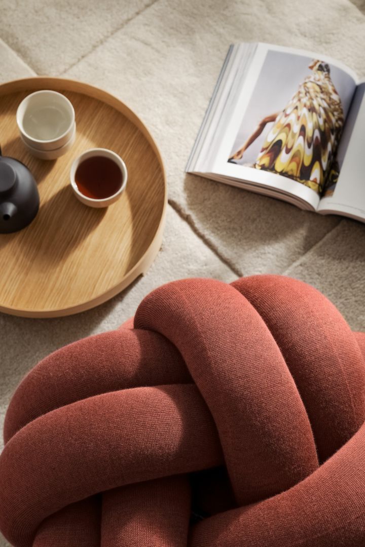 A close up of the Knot Cushion in ochre with a magazine, coffee cups and tea pot. 