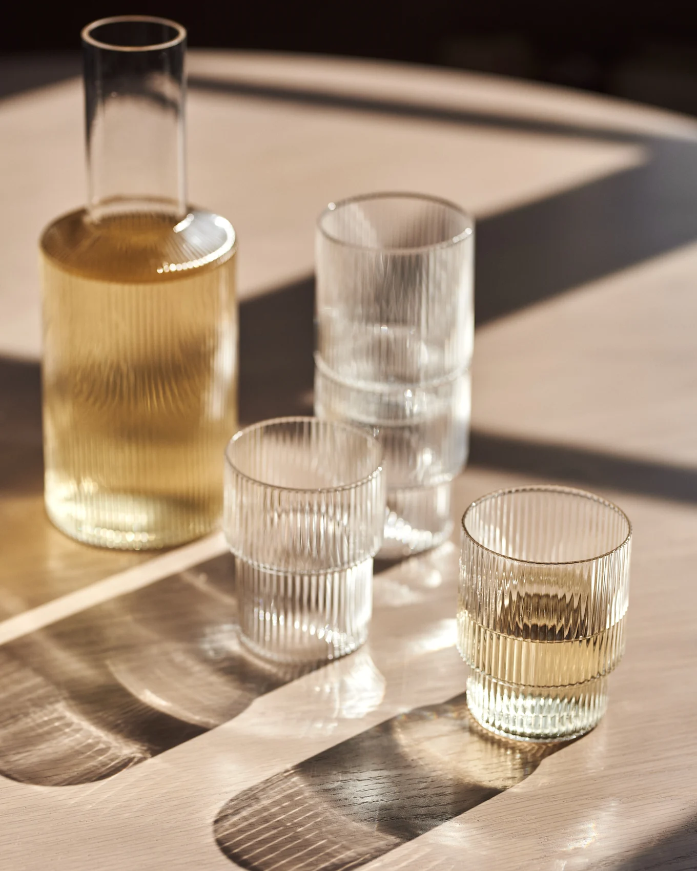 Glass carafe and ribbed tumblers on a wooden table with sunlight.