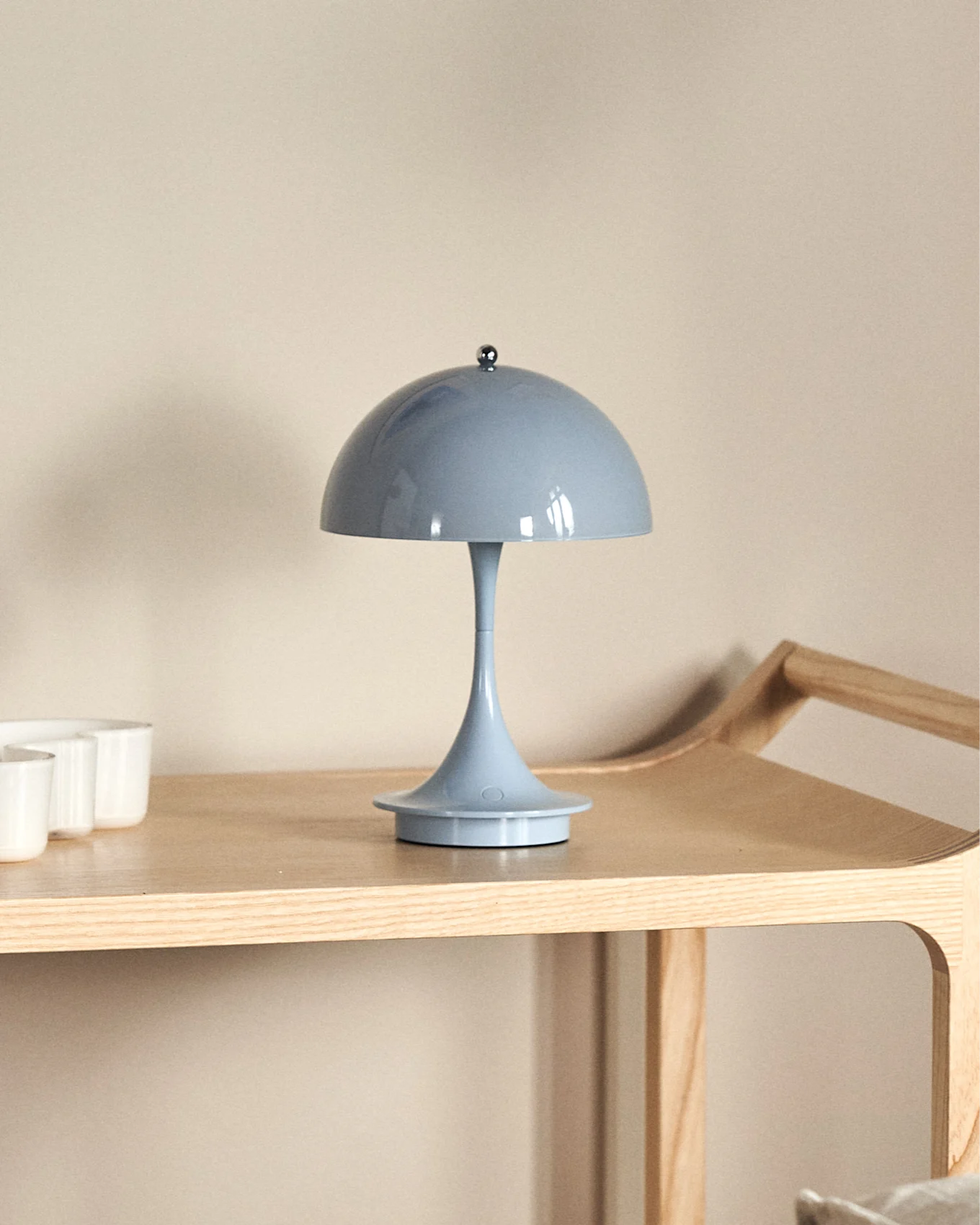 A light blue mushroom-shaped table lamp on a light wooden shelf, with white cups partially visible on the left.