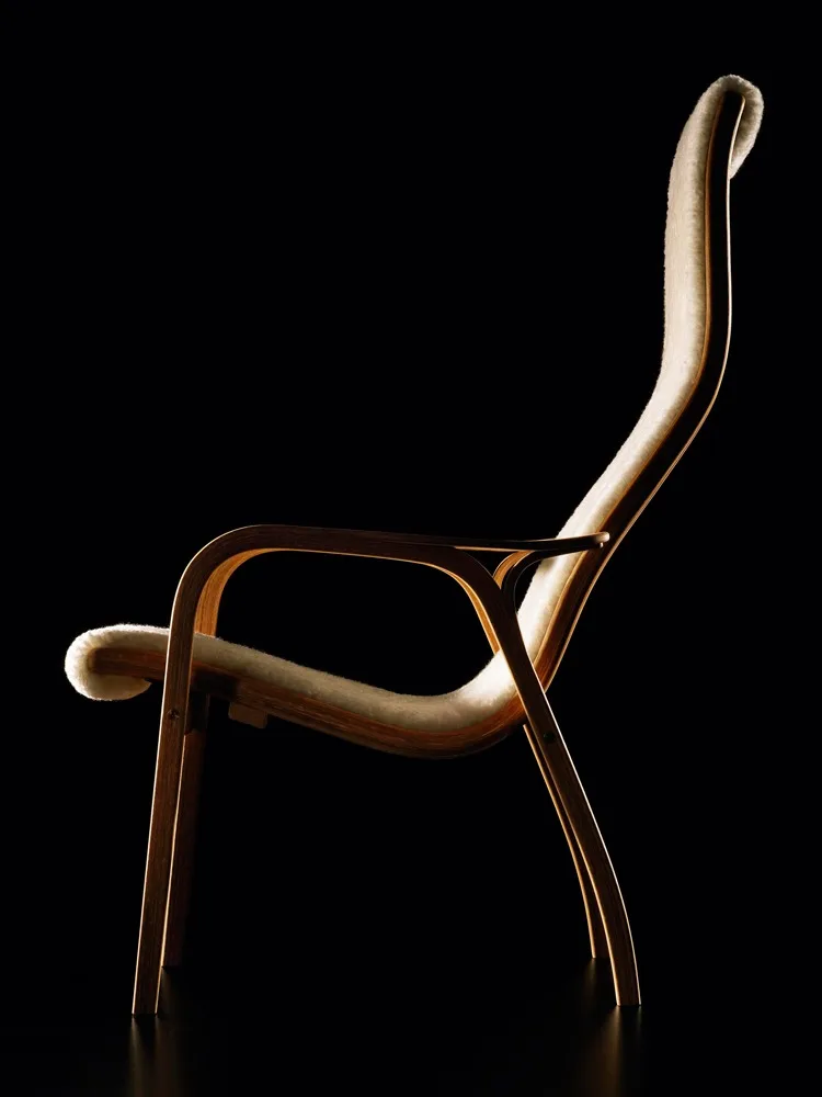 An elegant lounge chair with a curved light wood frame and cream furry upholstery, against a black background.