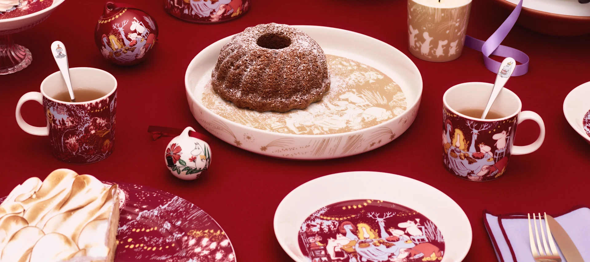 Various Moomin cups from Moomin Arabia stand on a table outside, next to a stamping jug.