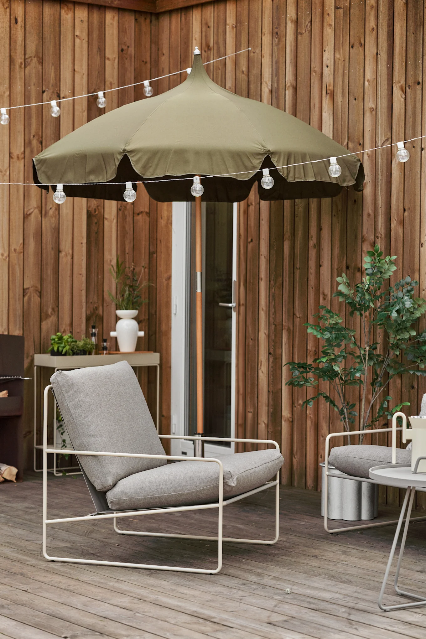 A cosy wooden terrace with fairy lights, Lull parasol and Desert lounge chair, both from Ferm Living.