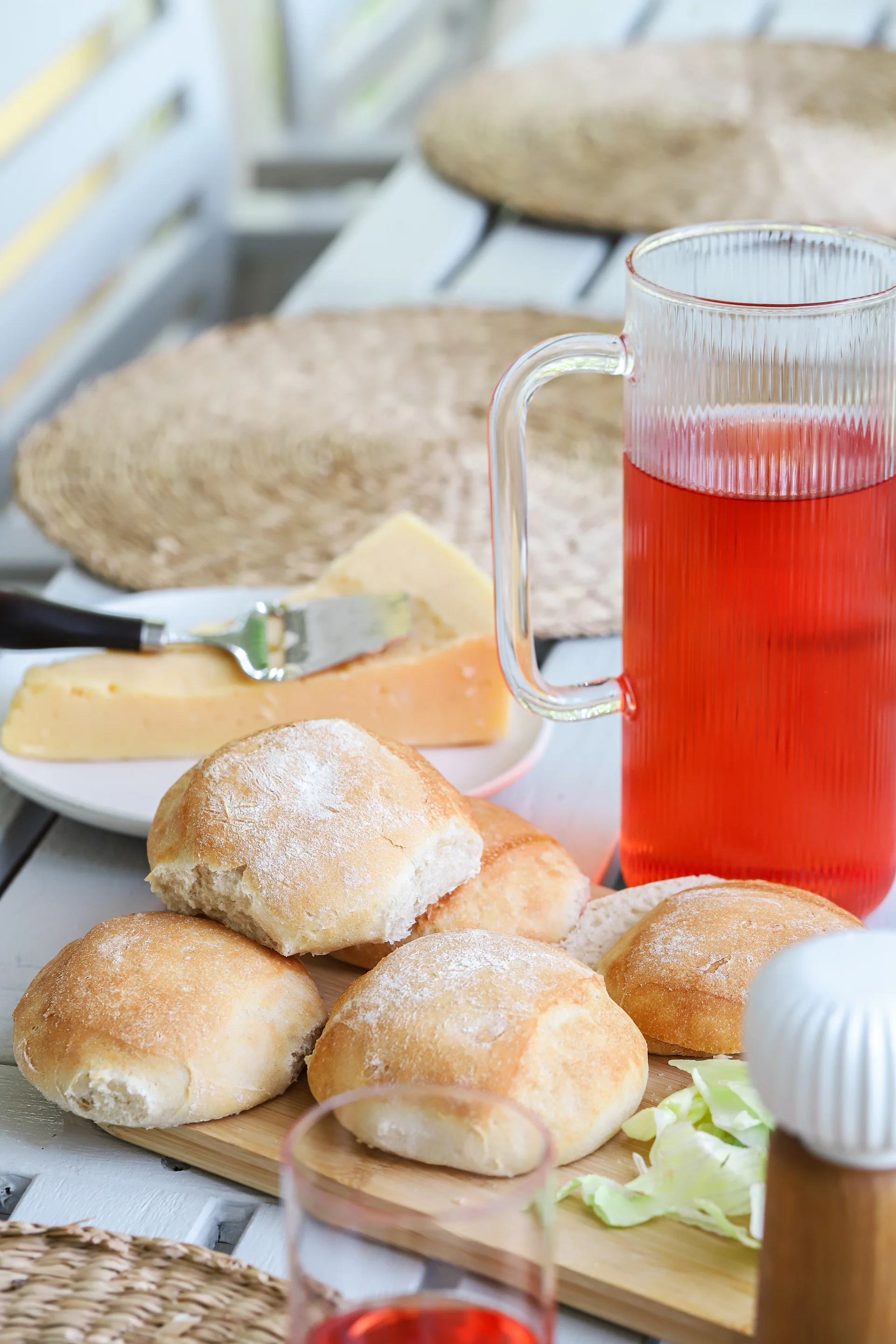 Picture showing freshly baked cold-fermented rolls, stacked on Nature cutting board in bamboo from Sagaform. In the background you can see Saga carafe and drinking glass.