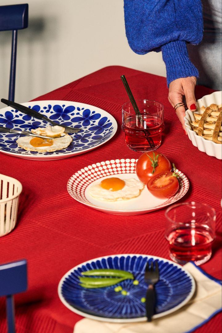 The interior colour trends for 2023 include red and blue in contrast. Here you see a table setting with blue Mon Amie plates from Swedish Rörstrand and a red tablecloth from NJRD. 