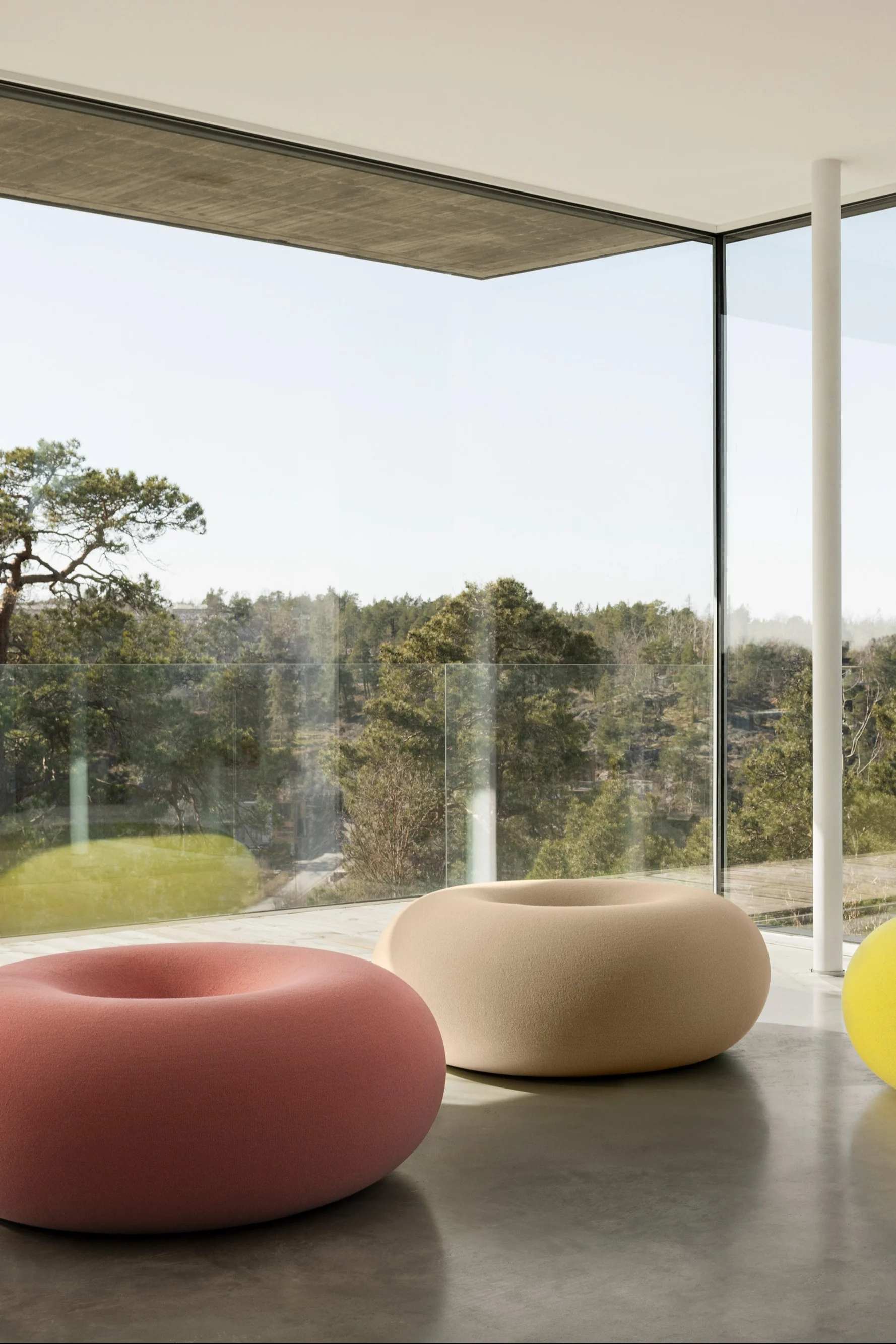A doughnut-shaped, colorful pouf placed in a minimalist room with large windows captures the essence of 2026 interior trends, serving as a playful yet refined focal point.