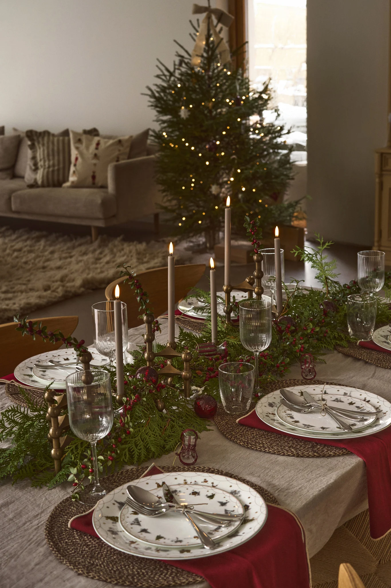 A Christmas table decorated with an Advent candle holder as the centrepiece, surrounded by fir branches and atmospheric Christmas details.