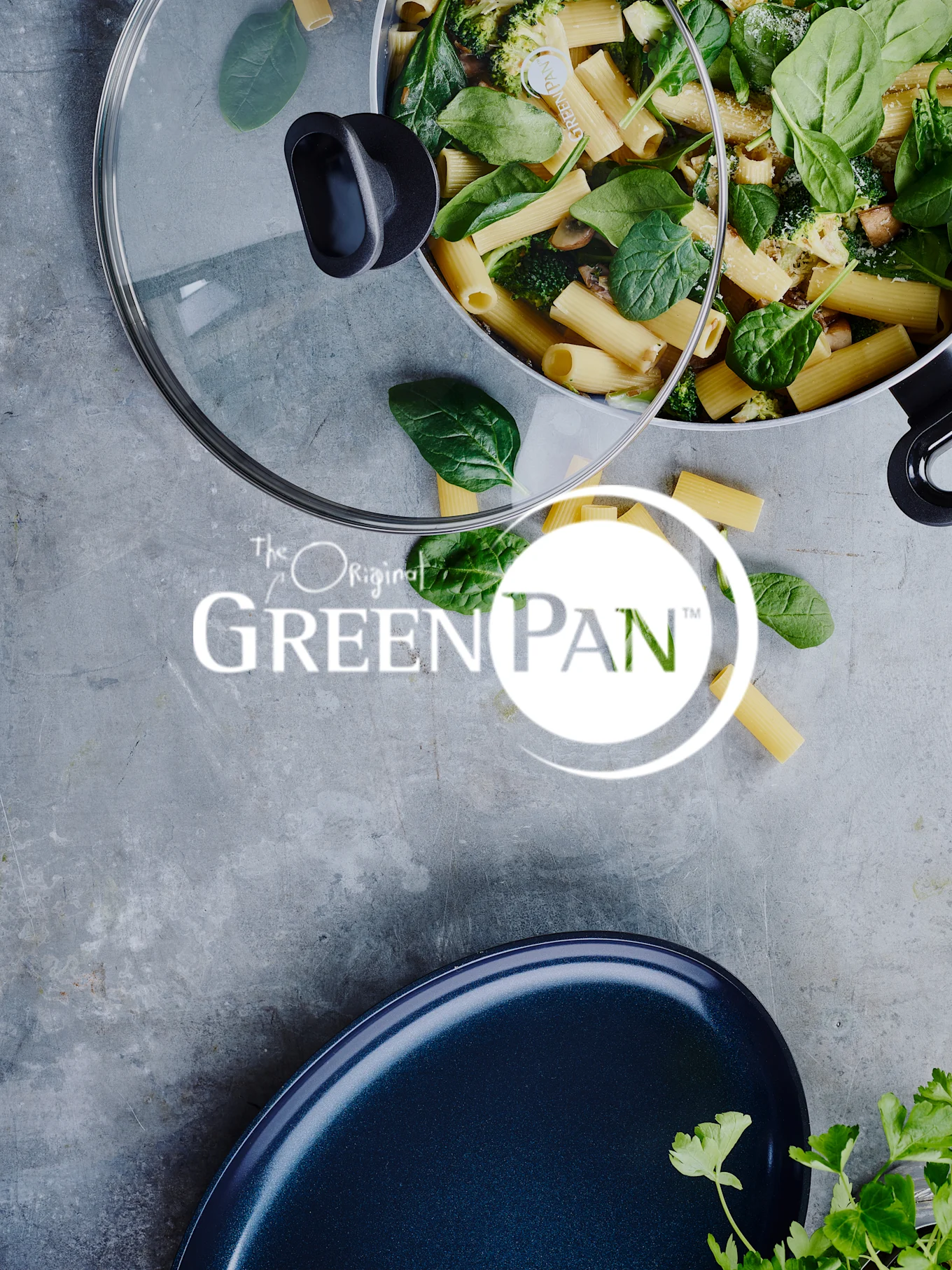 Pasta with spinach and broccoli in a pan, with a glass lid and the 'GreenPan' logo visible.