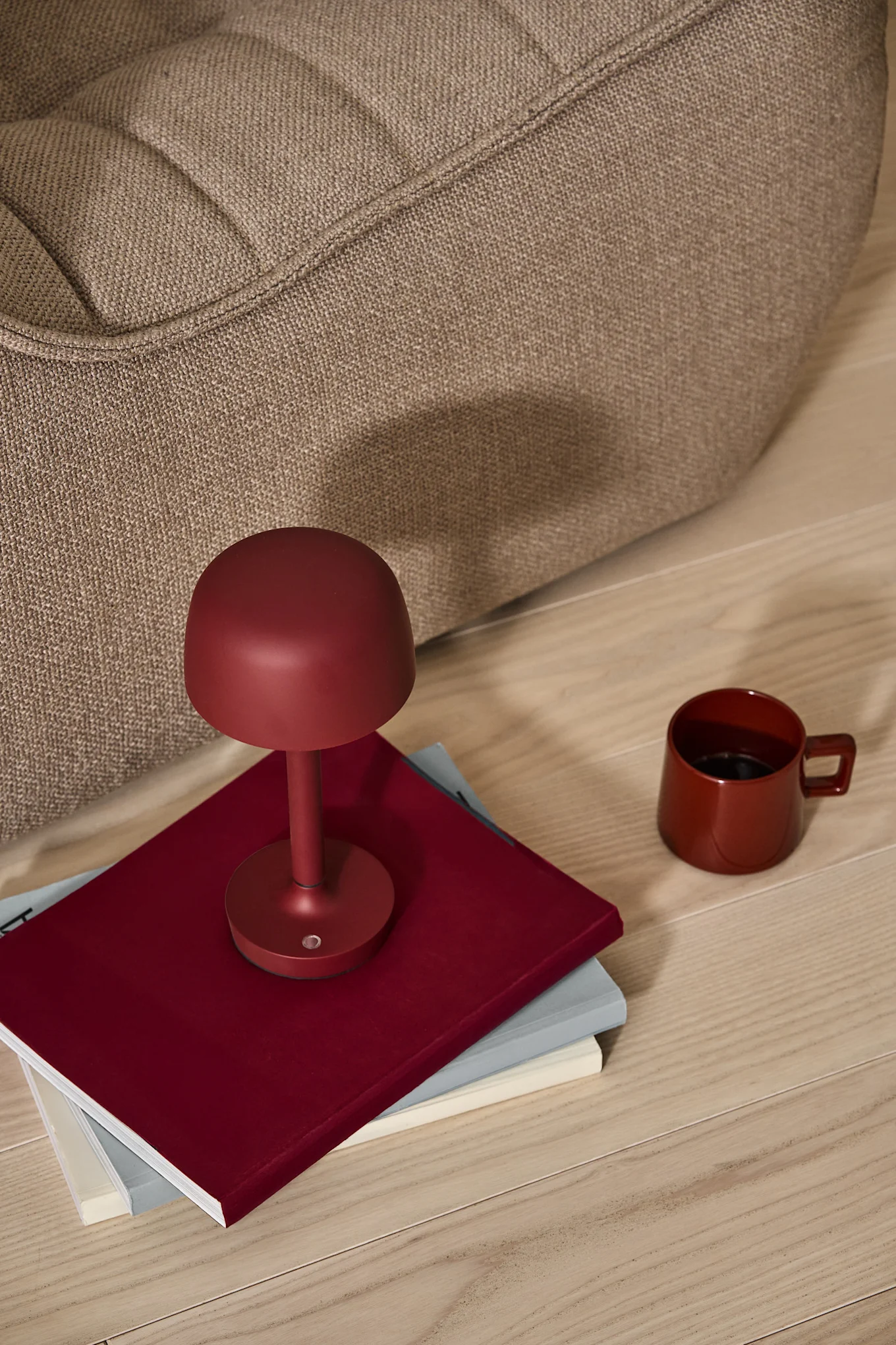 A dark red is one of the interior design trends for 2025. Here, the burgundy-coloured cordless Halo table lamp stands on a pile of books, next to the red Taper mug, both from Scandi Living.