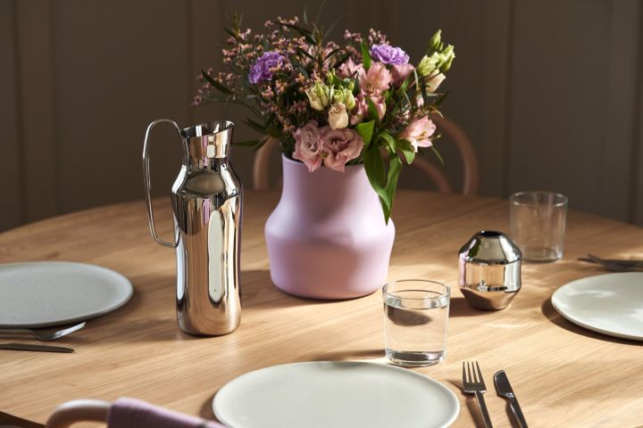 The polished stainless-steel water jug stands next to the lilac Dorotea vase designed by Monica Förster for Gense. 
