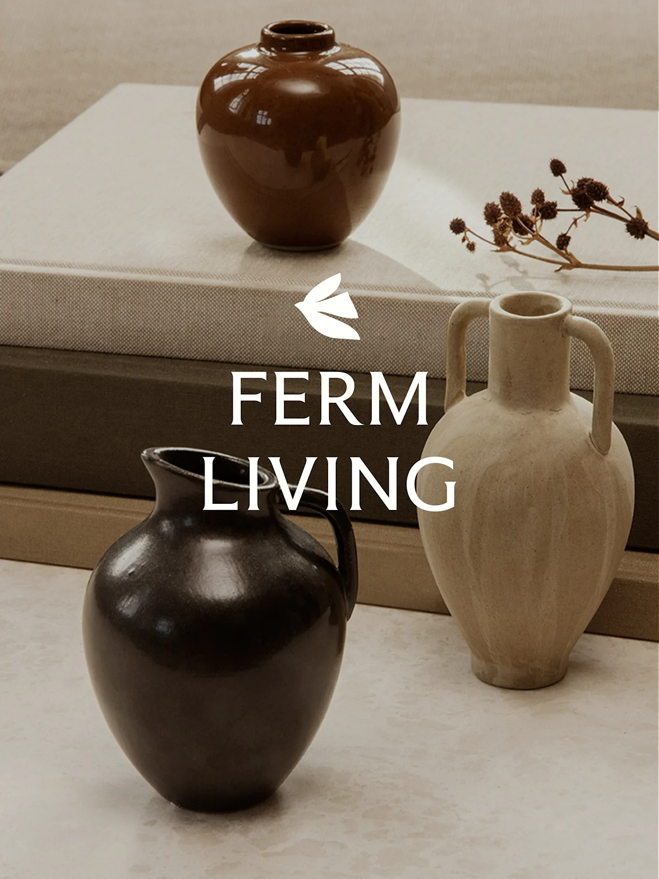 Three ceramic vases of different shapes and colors on stacked books, with dried plant stems.
