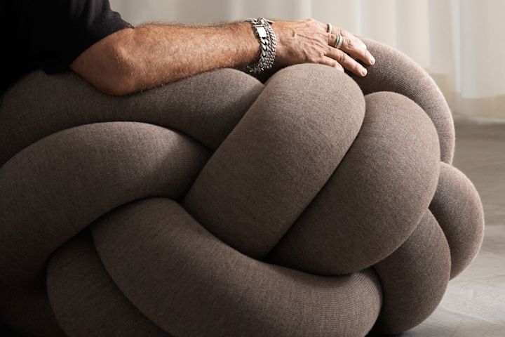 A man sits on top of the Knot Cushion XL in brown. 