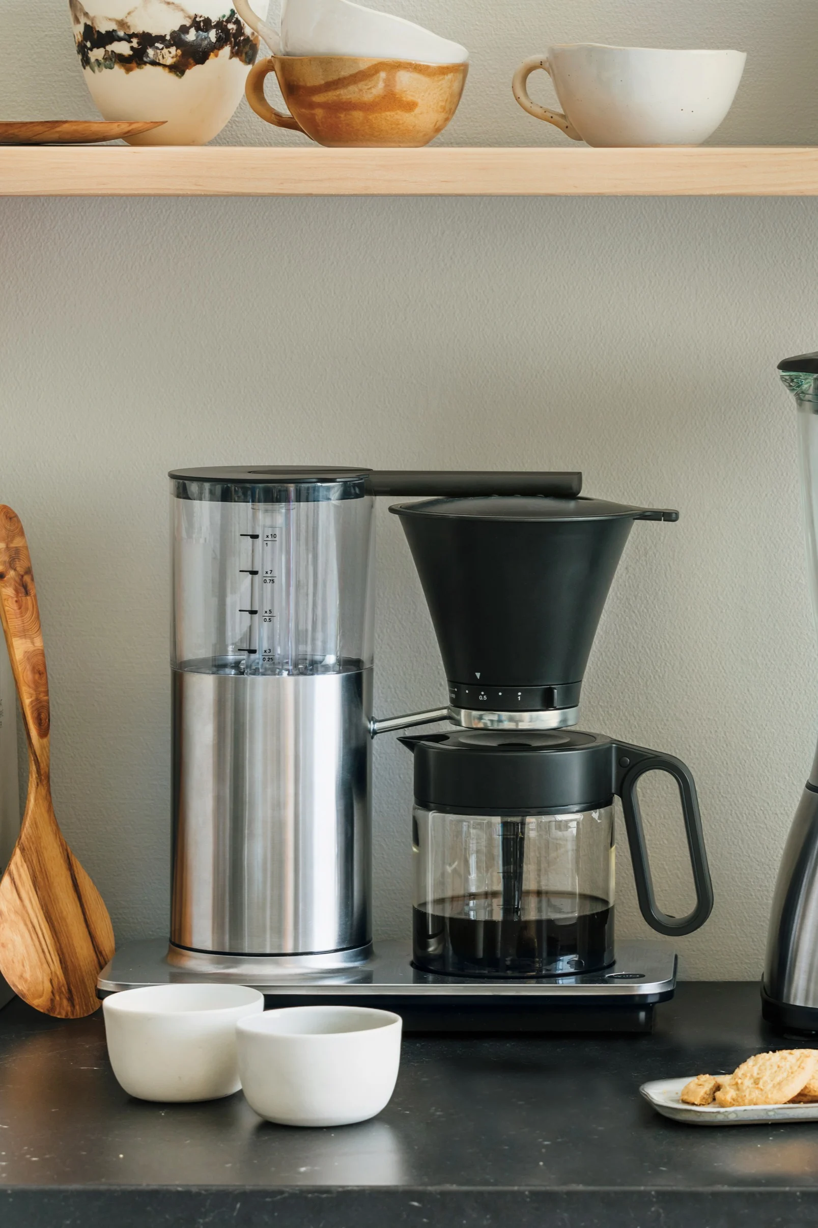 You also need the right appliances for your coffee bar at home. Here you can see a classic filter coffee machine from Wilfa standing on a kitchen sideboard, with a shelf with bowls and a toaster above it.