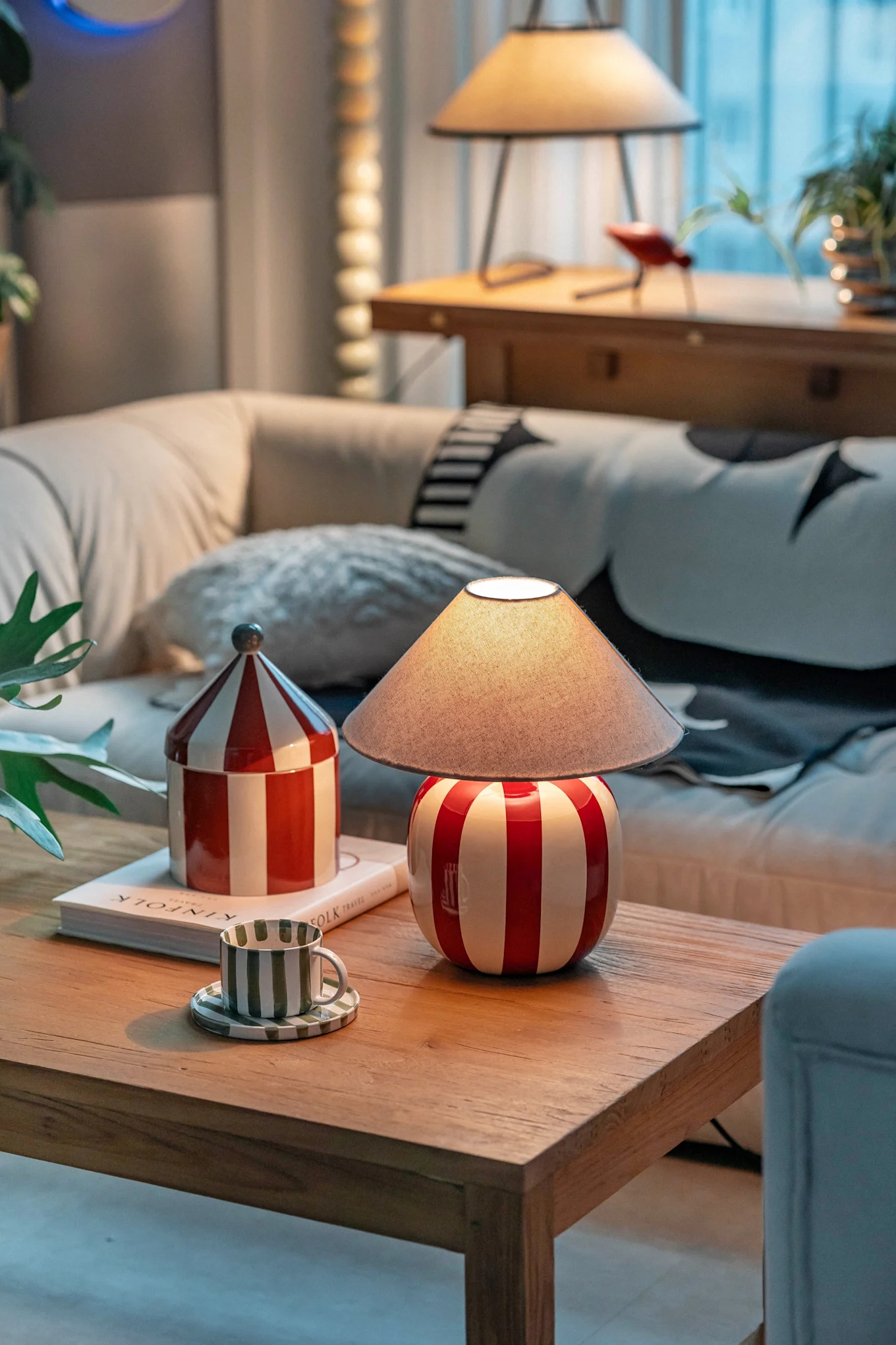 A cozy living room with a red and white striped lamp, matching canister, and a green striped cup on a wooden coffee table.
