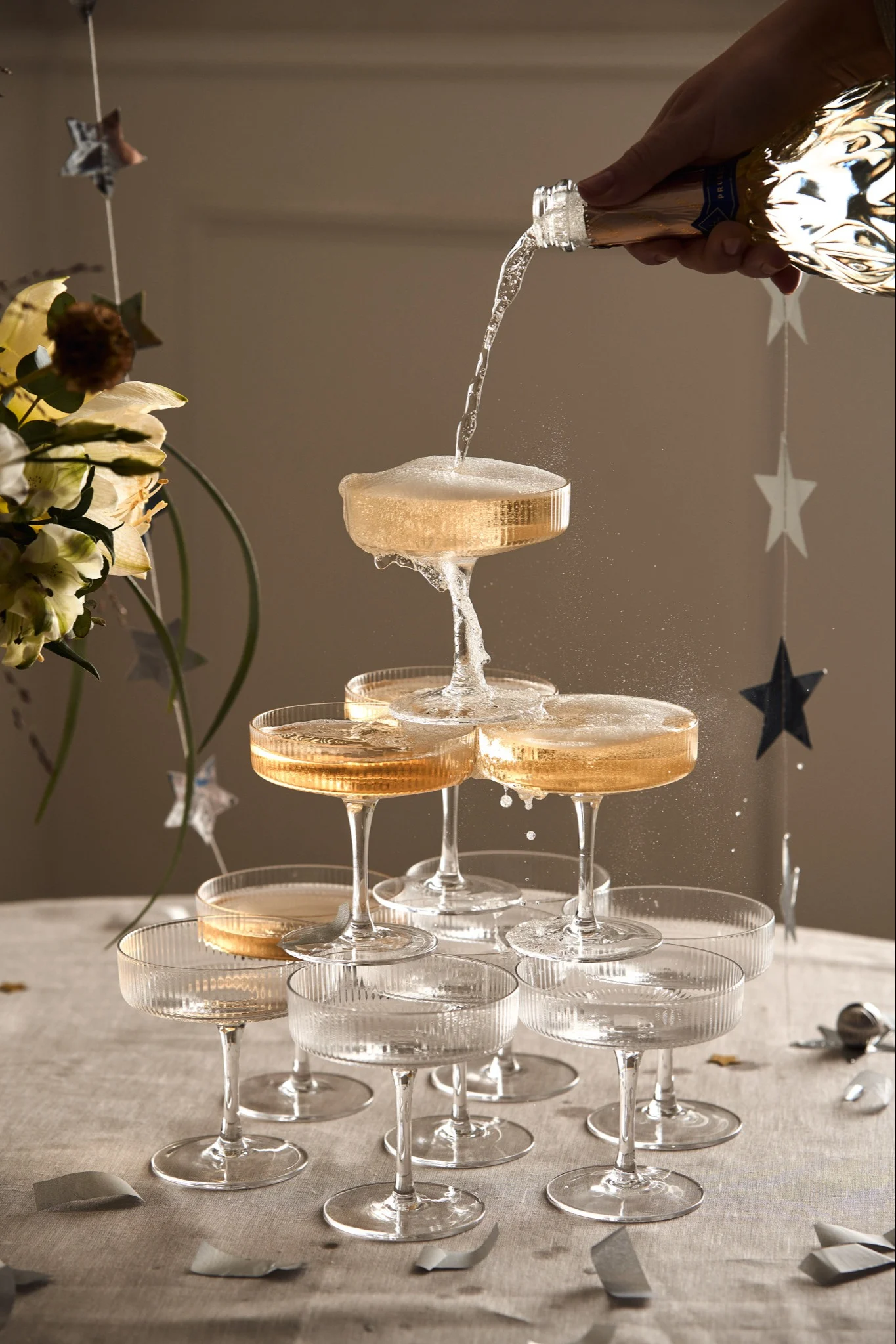 Learn how to build a champagne tower like the one you see here where a hand pours champagne into the top glass on a small champagne tower made with ripple champagne glasses.