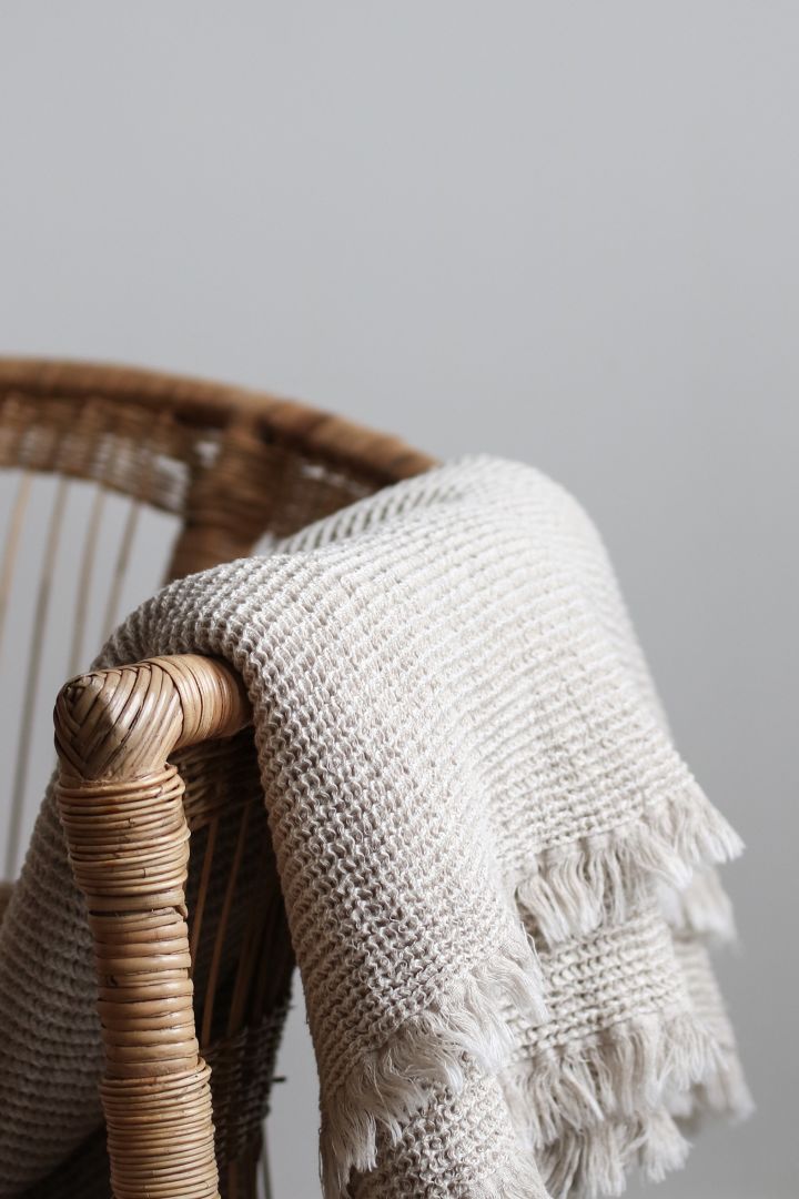Beige knitted Calma throw in cotton hangs over a dining chair for a cosy dining area. 