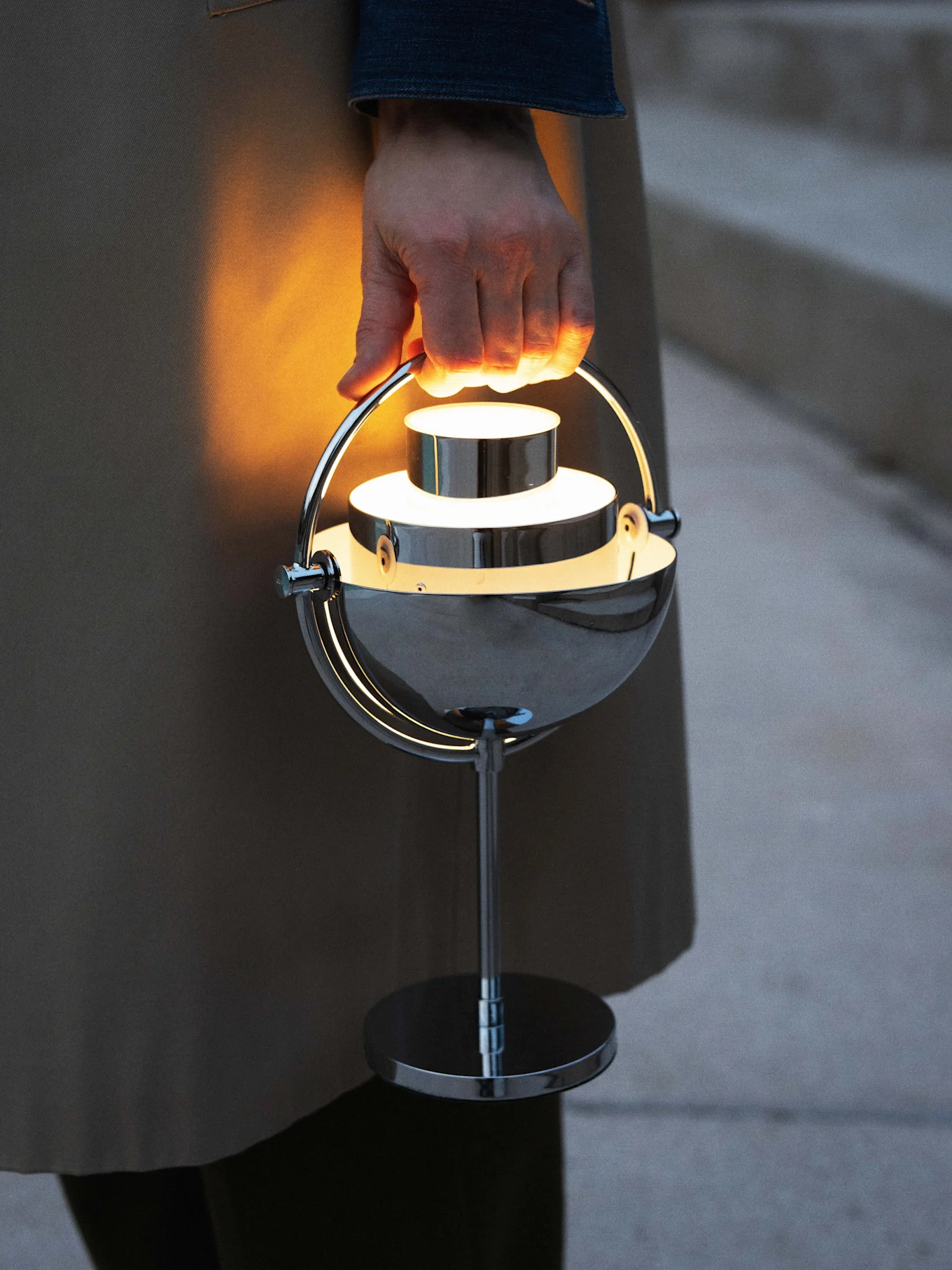 Hand holding a glowing, modern chrome portable lamp.