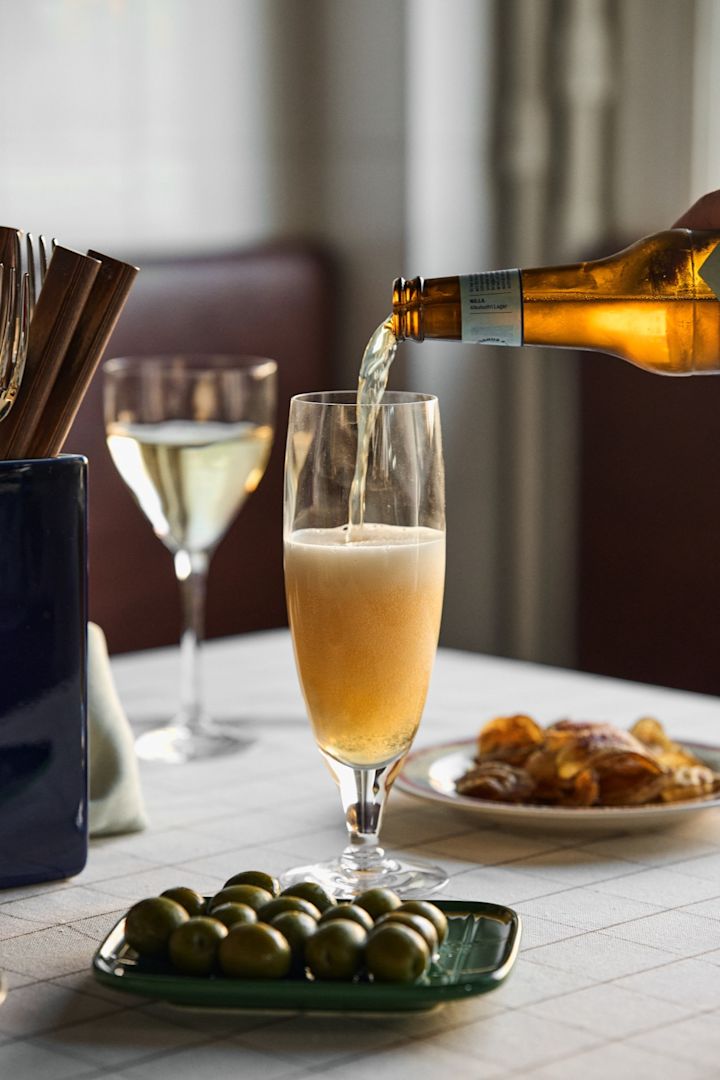 Learn how to choose the right beer glass. Here you see a beer being poured into the Chateau beer glass from Kosta Boda with a plate of olives next to the glass. 