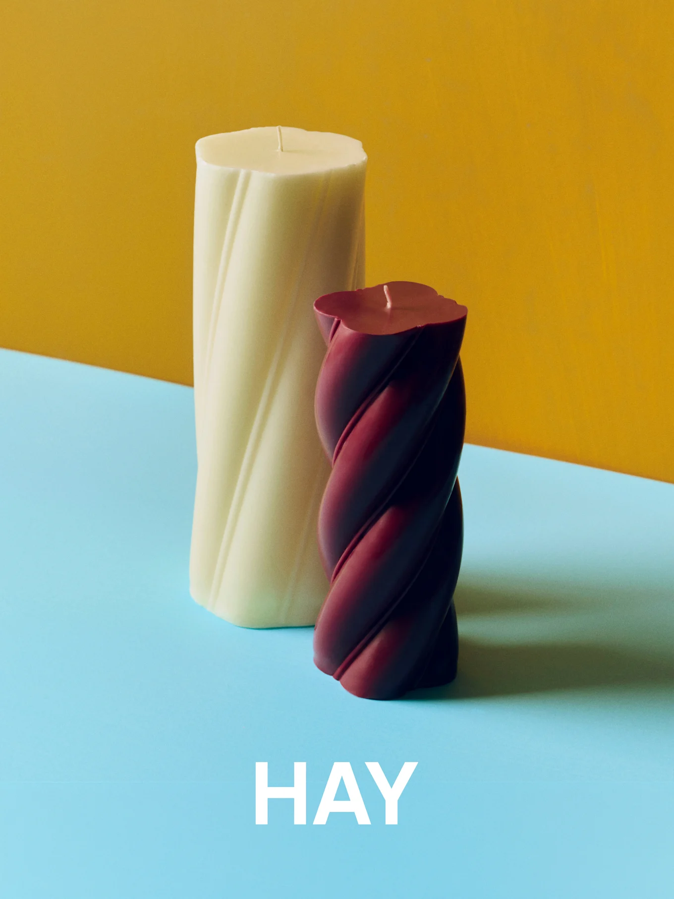 Cream and burgundy twisted candles on a yellow and blue background with 'HAY' text.