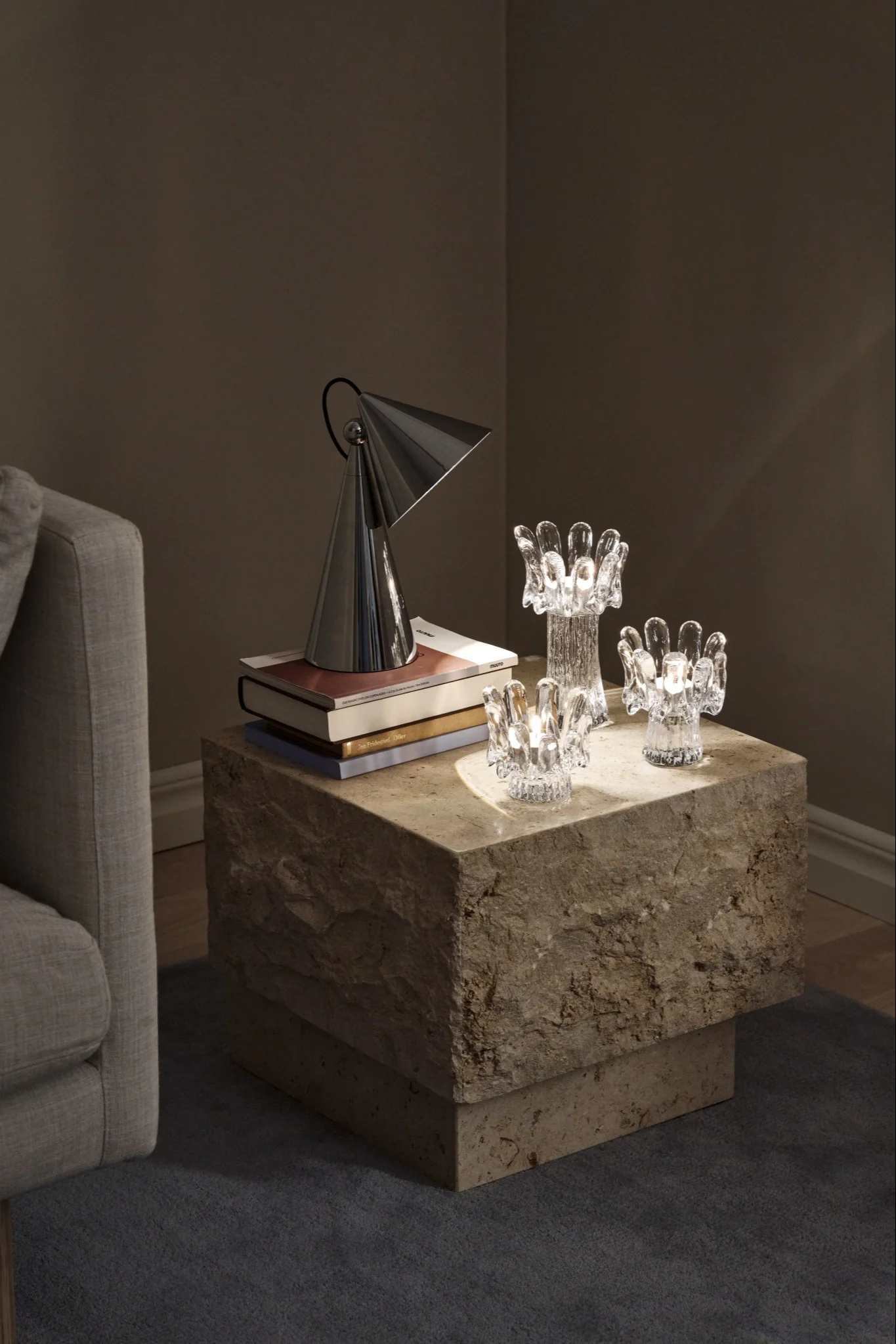 A dark setting illuminated by three glass candle holders shaped like sunflowers, placed on a stone table, a stylish hint at the interior design trends of 2026.