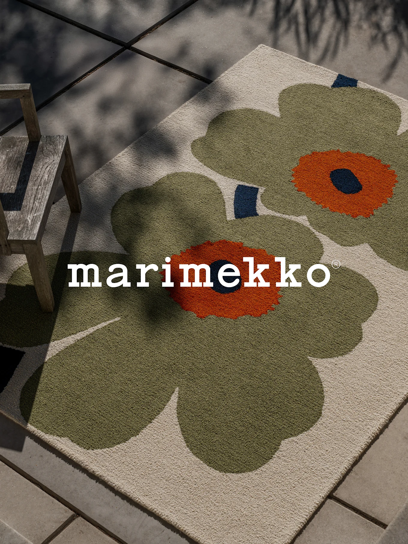 Marimekko rug with large green and orange floral pattern on a patio with a wooden chair.