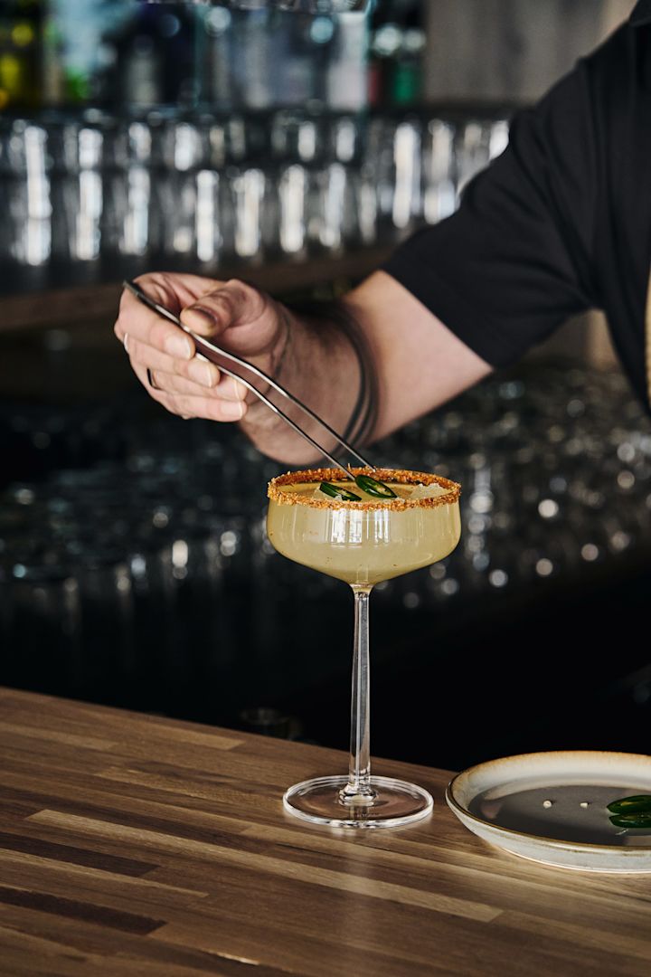 Perfect for mocktails: the Essence cocktail glass by Iittala with drink, decorated rim and garnished with jalapeño slices using tongs.