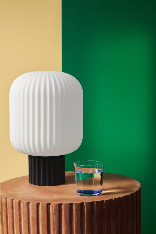 A table lamp in glass from Broste Copenhagen against a two toned wall in green and yellow. 