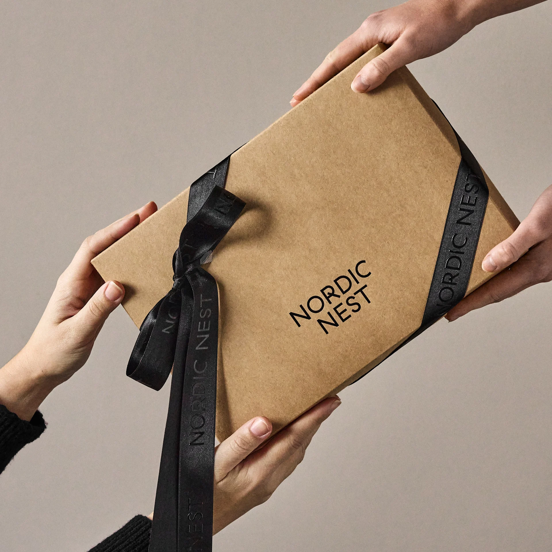 Hands exchanging a brown gift box with 'Nordic Nest' logo and black ribbon.