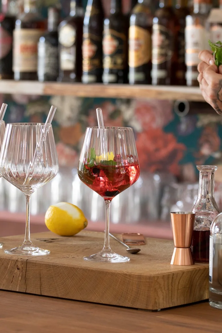A mocktail in a Nachtmann Feel Good G&T glass stands on a wooden board in front of a bar.