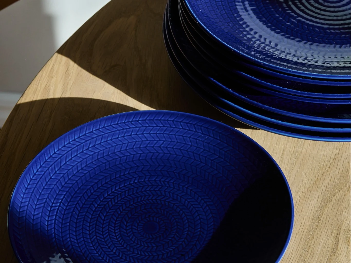 Deep blue textured plates on a wooden table, one in foreground, a stack behind.