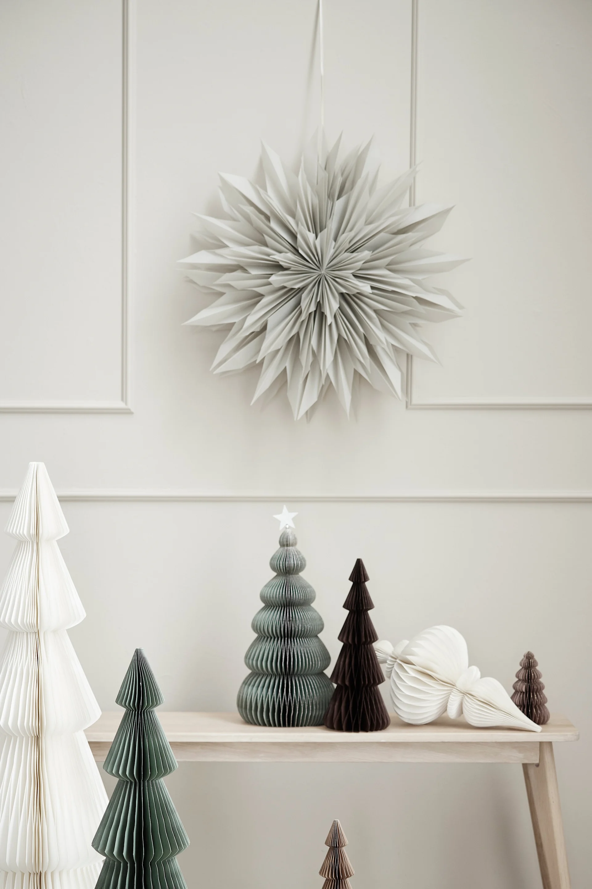 The paper star lantern Palisia from Lene Bjerre hangs over a wooden stool with paper trees arranged on it. 